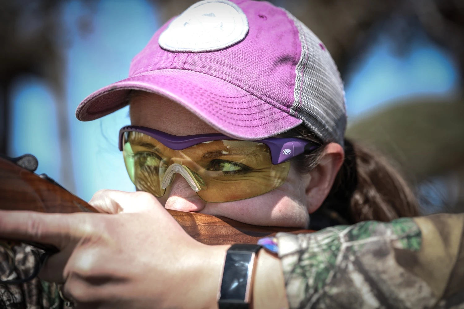 Shotgun shooter wearing purple Methow frames with yellow lenses, aiming away from the camera