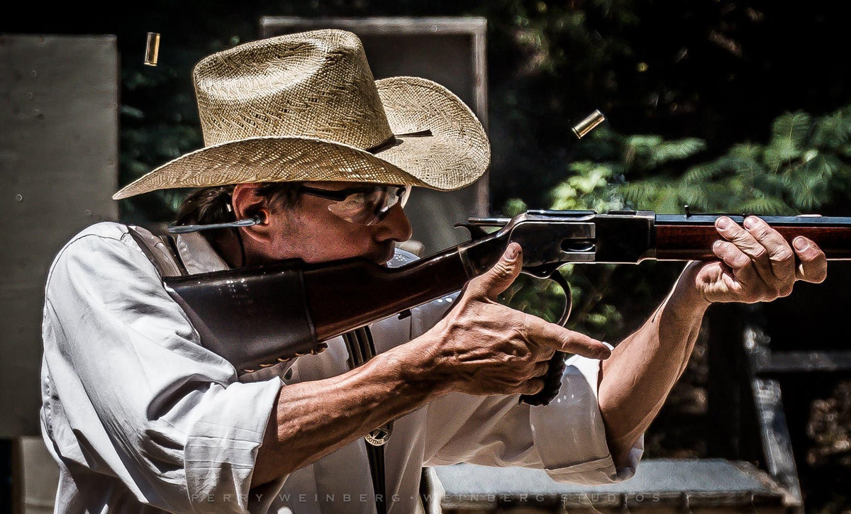 Cowboy action shooter wearing Denial eyewear while aiming a rifle outdoors.