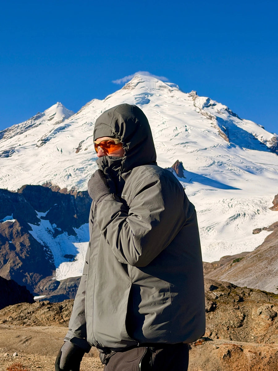 Roark standing in a hooded raincoat and orange Methow eyewear, looking toward the distance with Mount Baker behind him