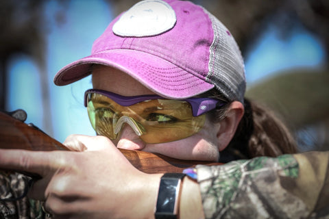 Woman aiming a shotgun in purple Methow frames with yellow lenses; lifestyle colorway